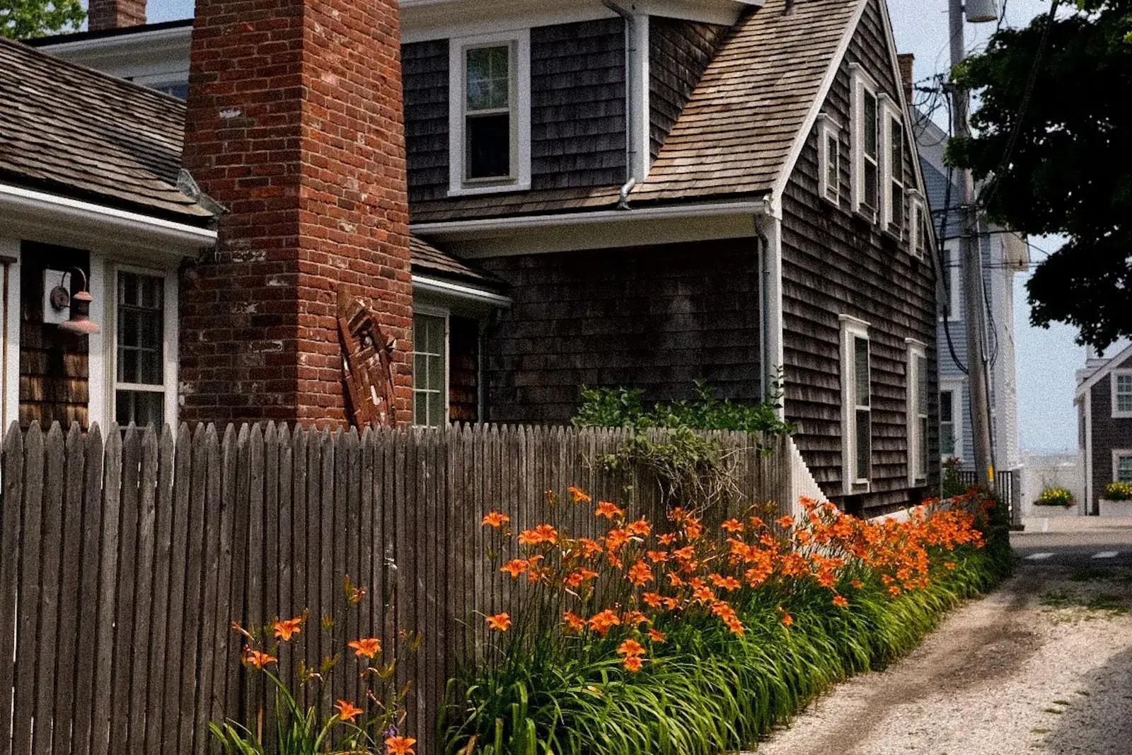 Old shingled house with a brick chimney and a wooden fence