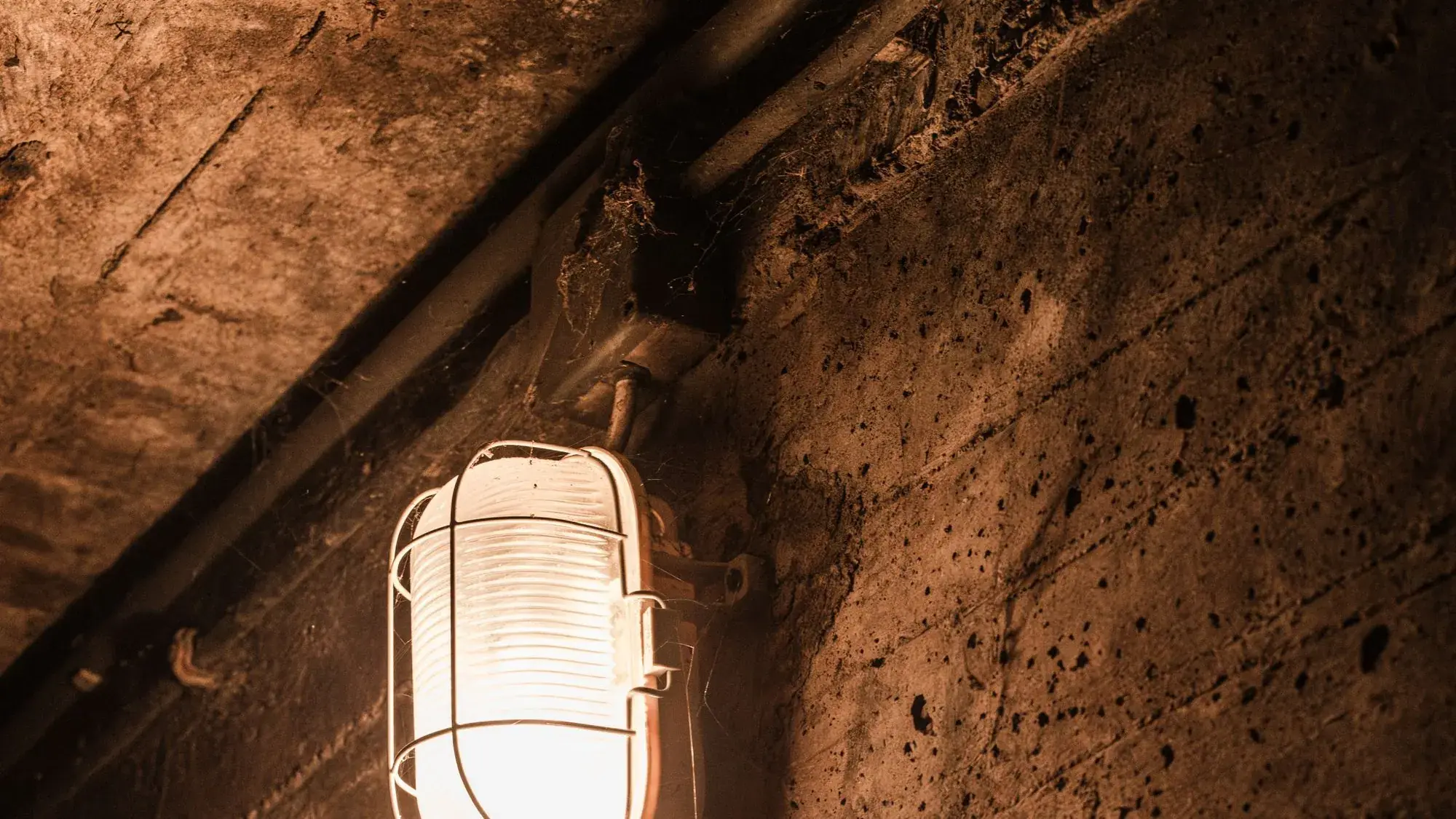 Poured concrete basement wall lit by a caged bulkhead light